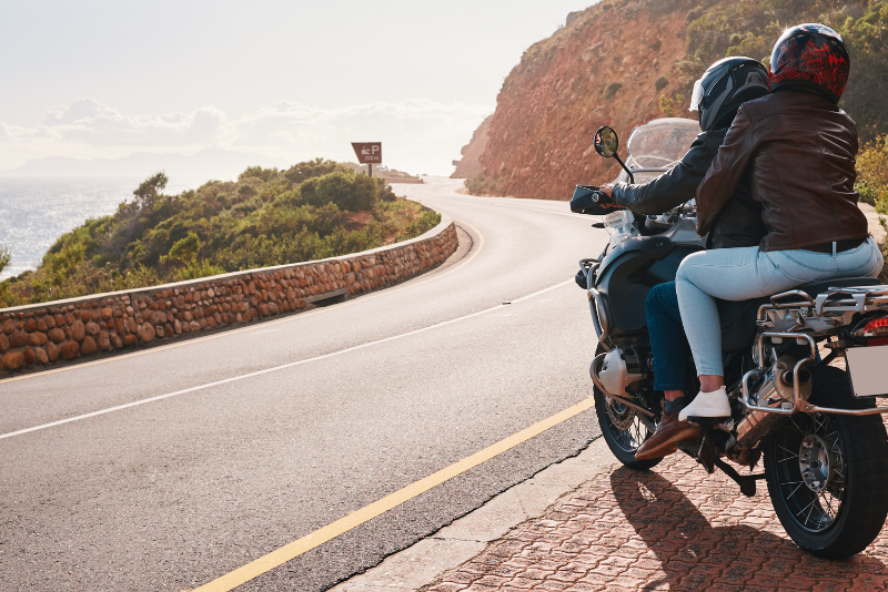 Motorrad im Ausland Motorradfahrer mit Sozius auf einer kurvigen Küstenstraße im Ausland bei sonnigem Wetter während einer Motorradtour.